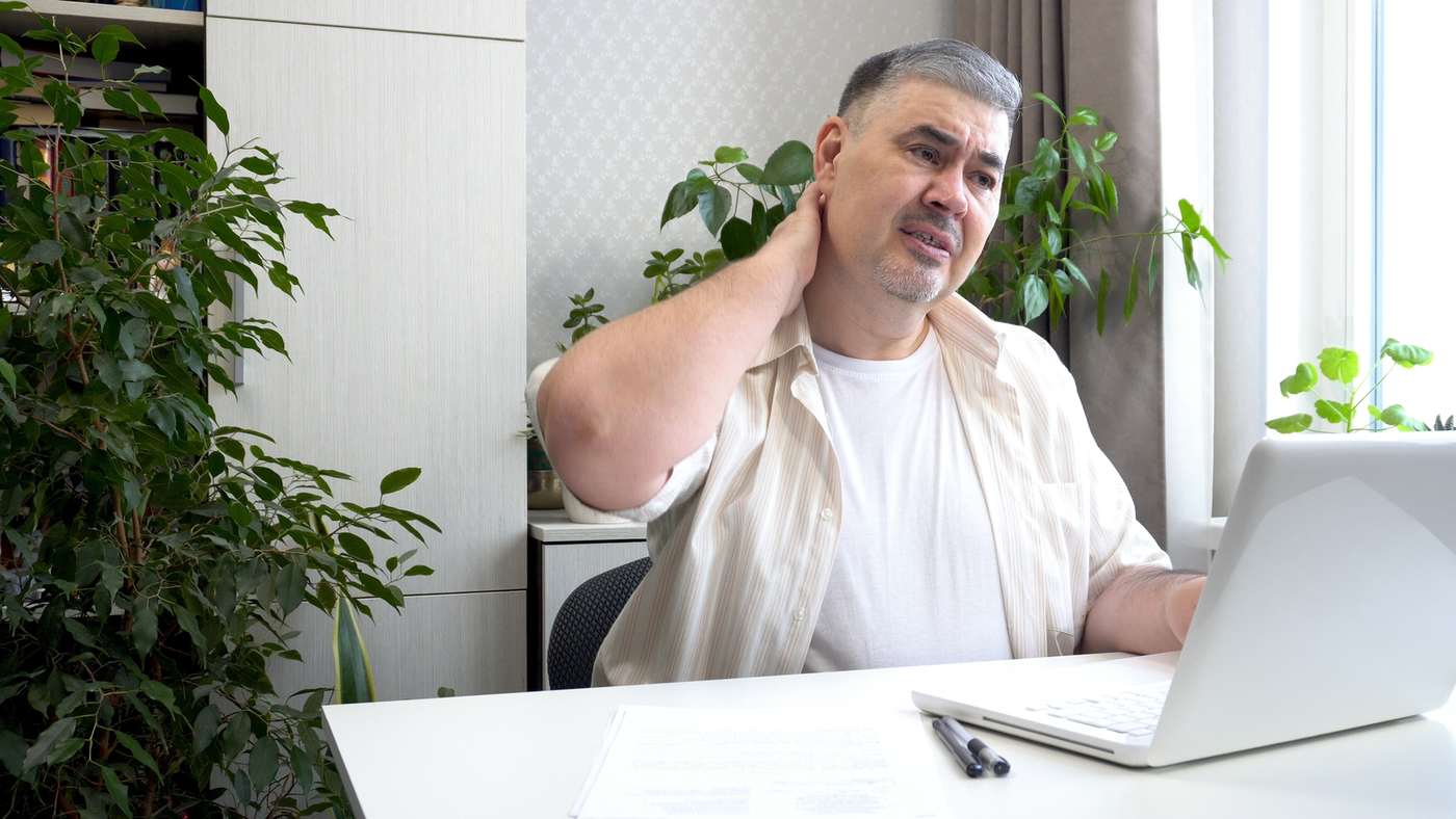 Man at a desk holding his neck in discomfort from long hours of office work.