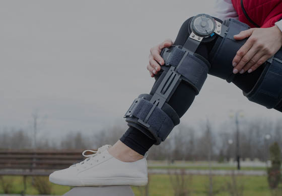 Young woman's leg equipped with a custom brace, her foot is up on a bench in the park