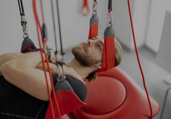 Young man laying on his back in a Red Cord suspension system with his arms crossed over his chest and on his shoulders