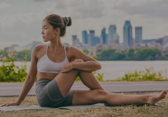 Young, fit woman sitting in a park doing a twisted yoga pose