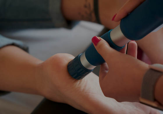 Young female practitioner doing shockwave therapy on the bottom of the patient's foot